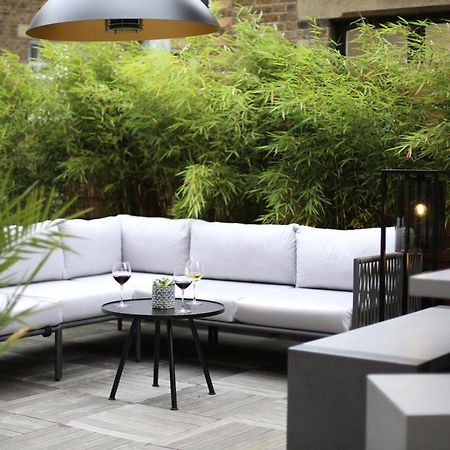 Middle Eight - Covent Garden - Preferred Hotels And Resorts London Exteriör bild The photo shows an outdoor seating area featuring a modern gray sectional sofa with plush cushions. In front of the sofa is a small, round black table with two glasses of wine on it, accompanied by a decorative plant or vase. Surrounding the area are
