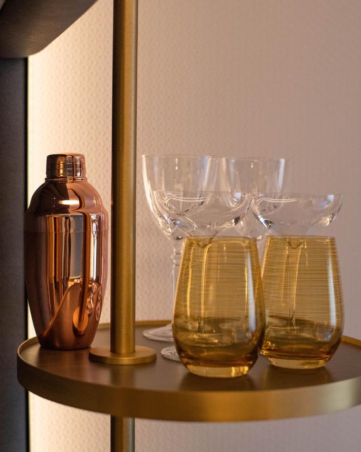 Middle Eight - Covent Garden - Preferred Hotels And Resorts London Exteriör bild The photo shows a stylish bar setup featuring a shiny copper cocktail shaker positioned next to several elegant glassware pieces. There are four tall, clear stemmed glasses and two round, amber-colored glasses with a textured pattern. The background 
