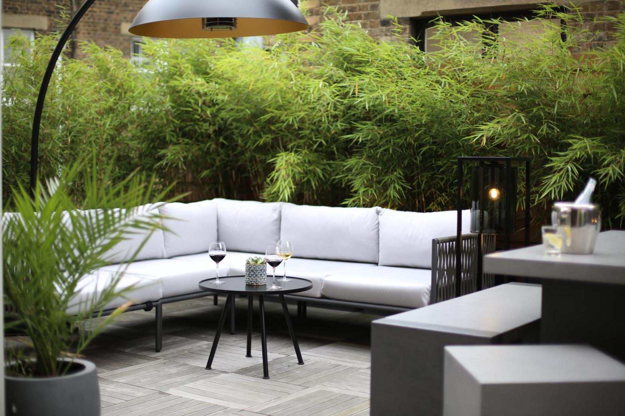 Middle Eight - Covent Garden - Preferred Hotels And Resorts London Exteriör bild The photo shows an outdoor seating area featuring a modern gray sectional sofa with plush cushions. In front of the sofa is a small, round black table with two glasses of wine on it, accompanied by a decorative plant or vase. Surrounding the area are